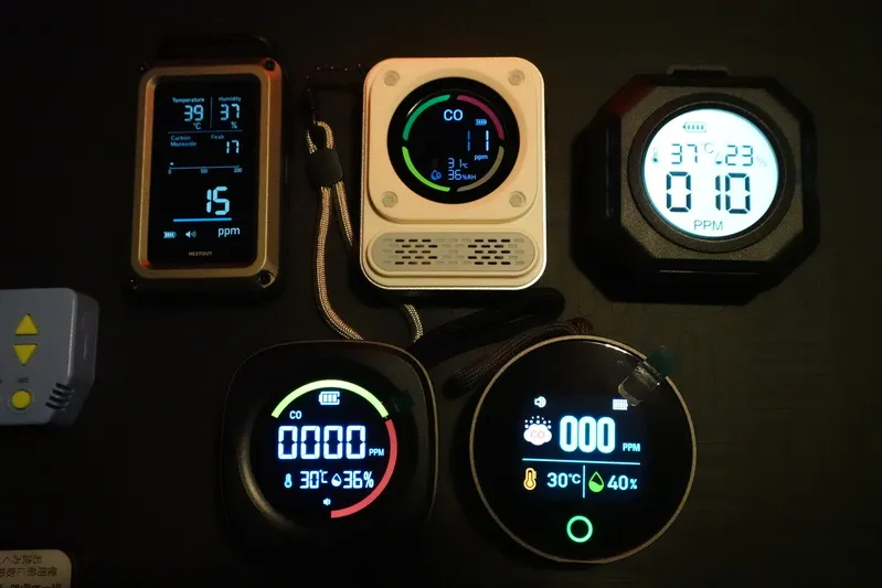 カセットガスストーブ前で一酸化炭素チェッカー3機種（エレコム・BOSEAN・モノンズ）が10〜15ppmを表示し、他モデルは0ppmのままの比較検証シーン